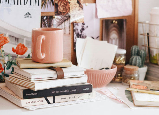 Books stacked on desk with pink mug